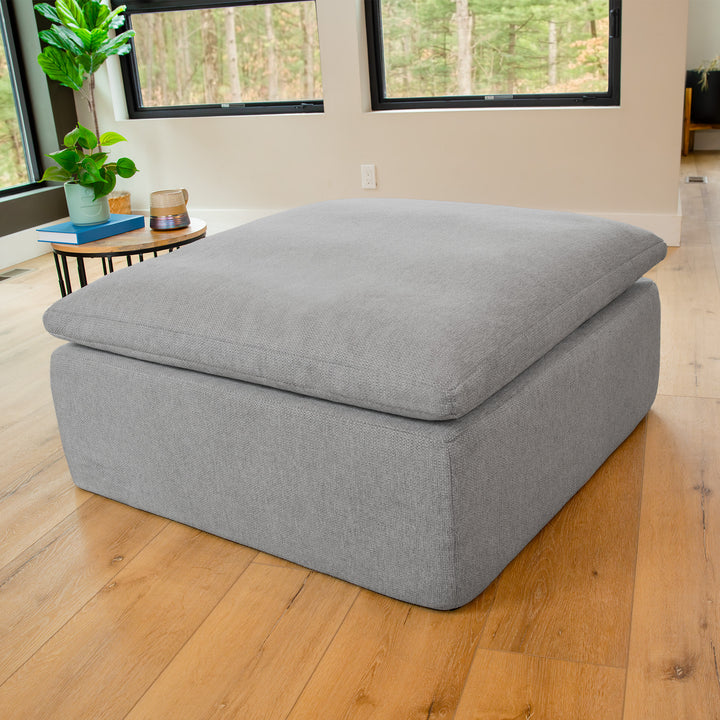 Gray ottoman in a room with wooden floor and large windows 