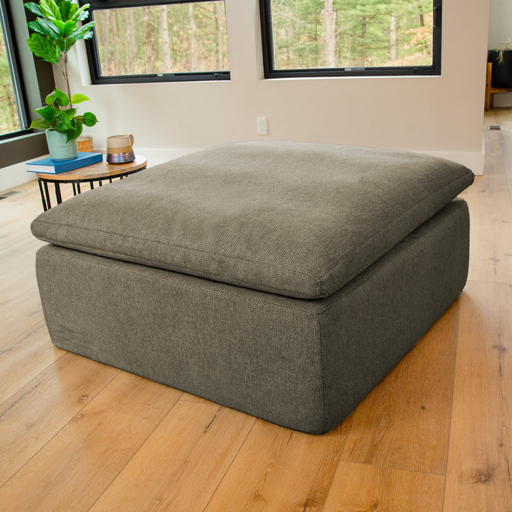 Gray ottoman in a room with wooden floor and large windows 