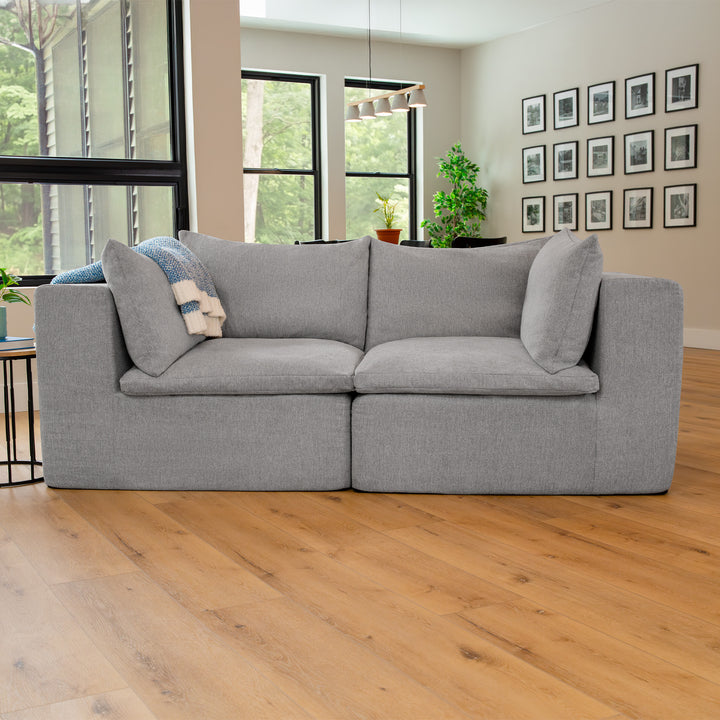Gray sofa in a living room with large windows and framed pictures on the wall. 