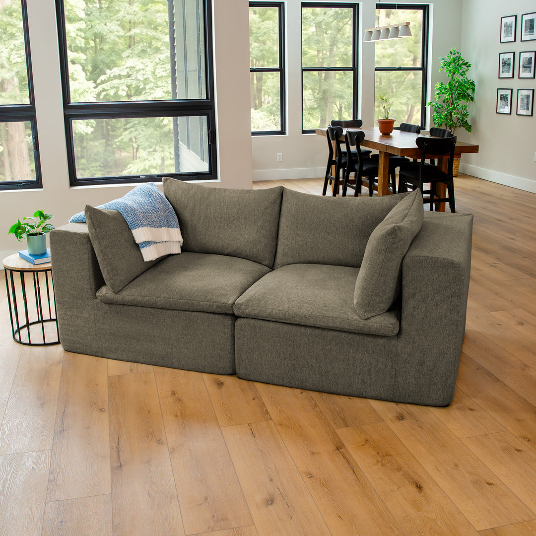 Gray sofa in a living room with large windows and a dining area in the background. 