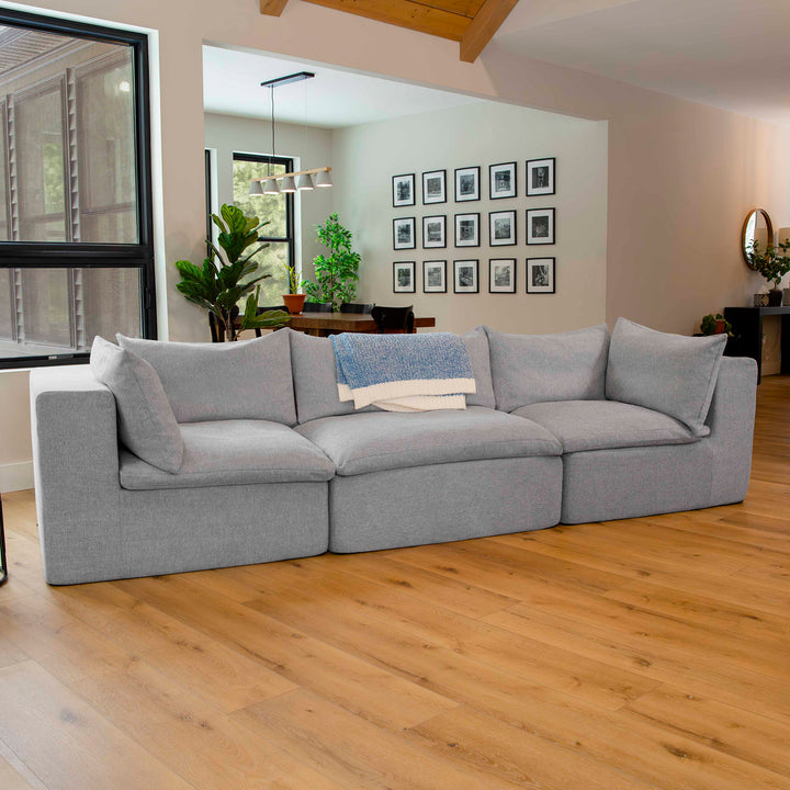 Gray sectional sofa in a living room with wooden floor and framed pictures on the wall. 