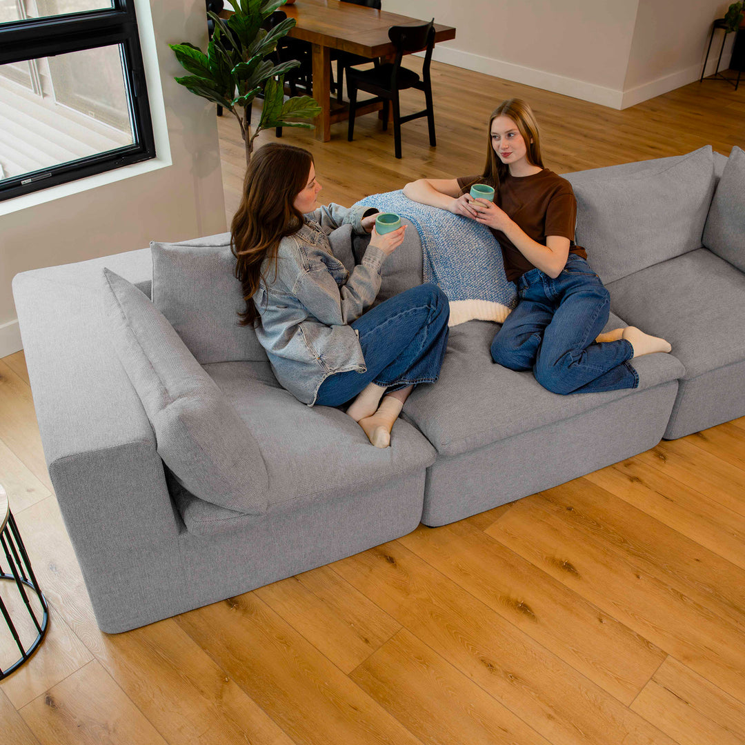 Two women sitting on a gray sectional sofa in a living room. 