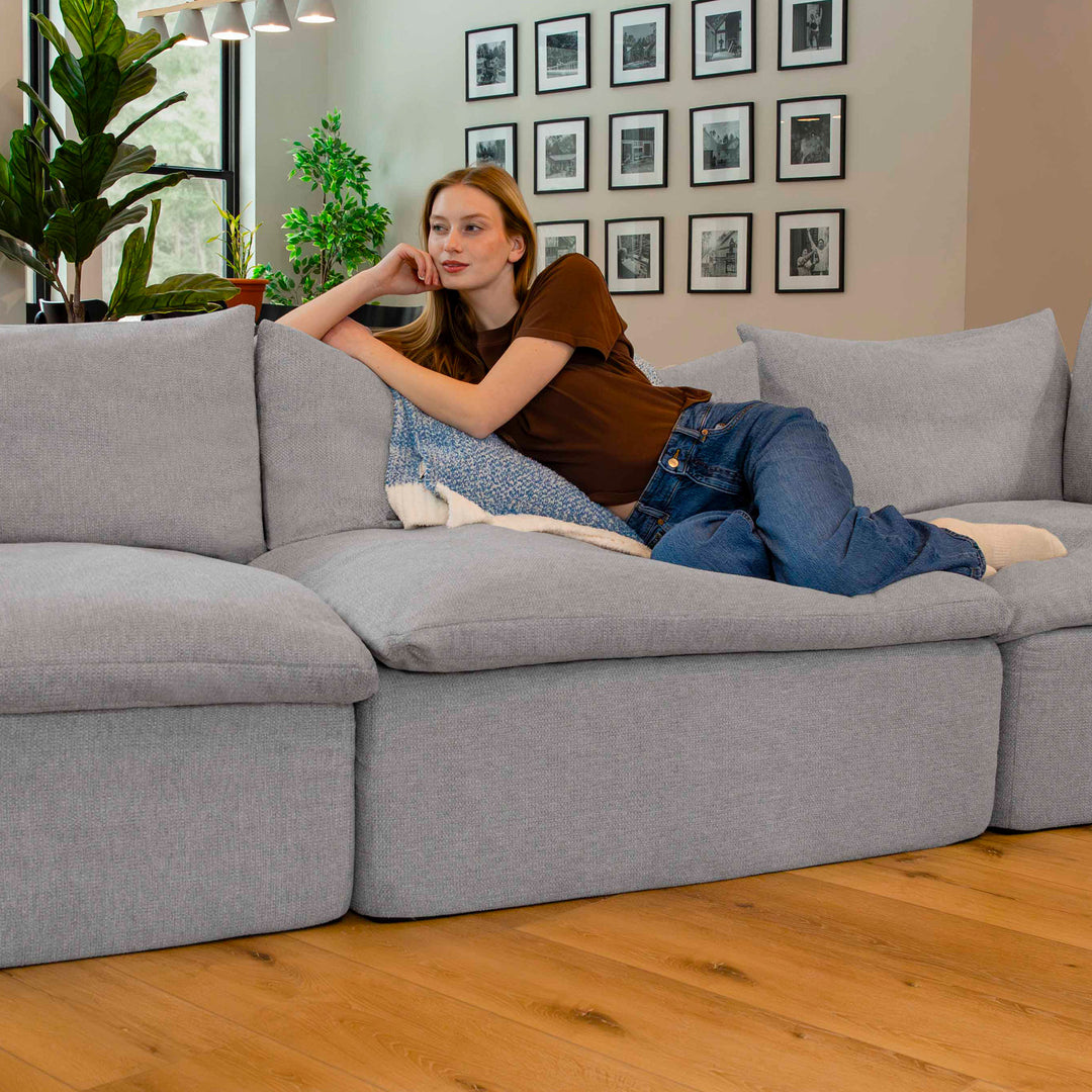 Woman lying on a gray sectional sofa in a living room with framed pictures on the wall. 