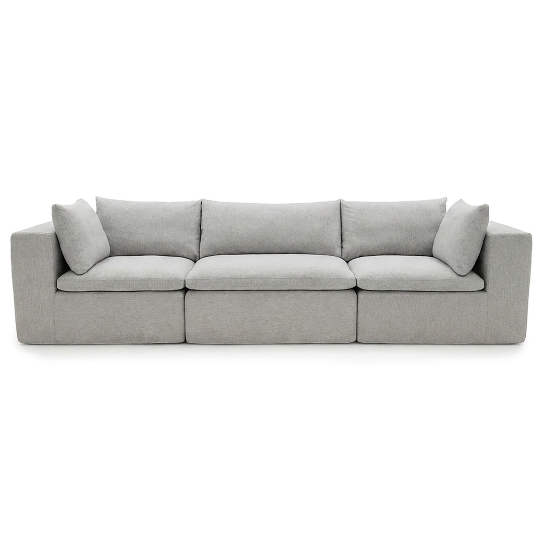 A modern three-seater sofa upholstered in light gray fabric, featuring segmented seat cushions and two matching back cushions, shown against a plain white background. 