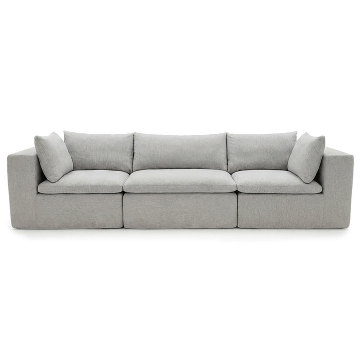 A modern three-seater sofa upholstered in light gray fabric, featuring segmented seat cushions and two matching back cushions, shown against a plain white background. 