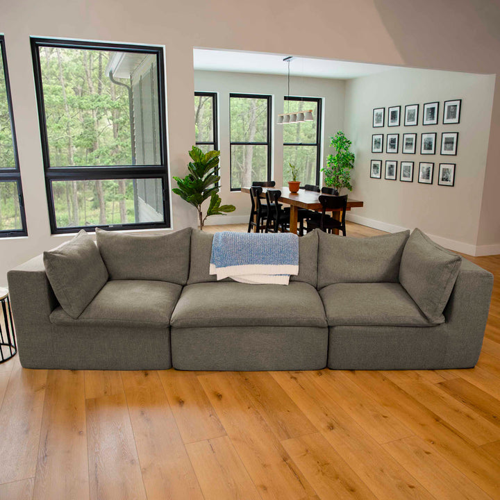 Gray sectional sofa in a living room with large windows and a dining area. 