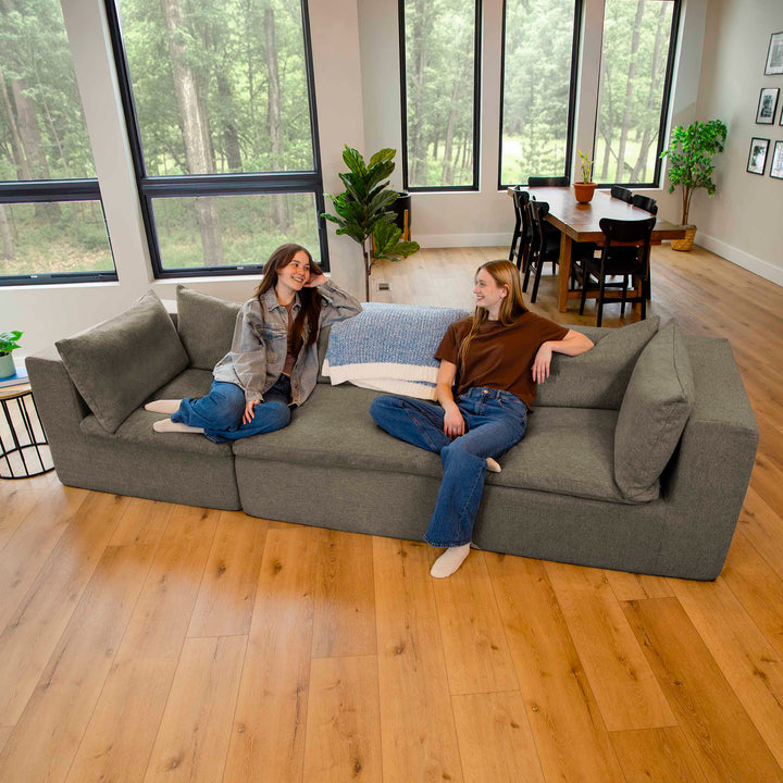 Two people sitting on a gray sofa in a modern living room with large windows and wooden flooring. 