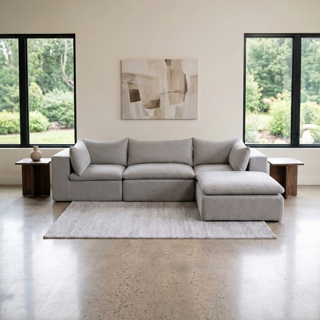 Gray sectional sofa in a modern living room with large windows and abstract art on the wall. 