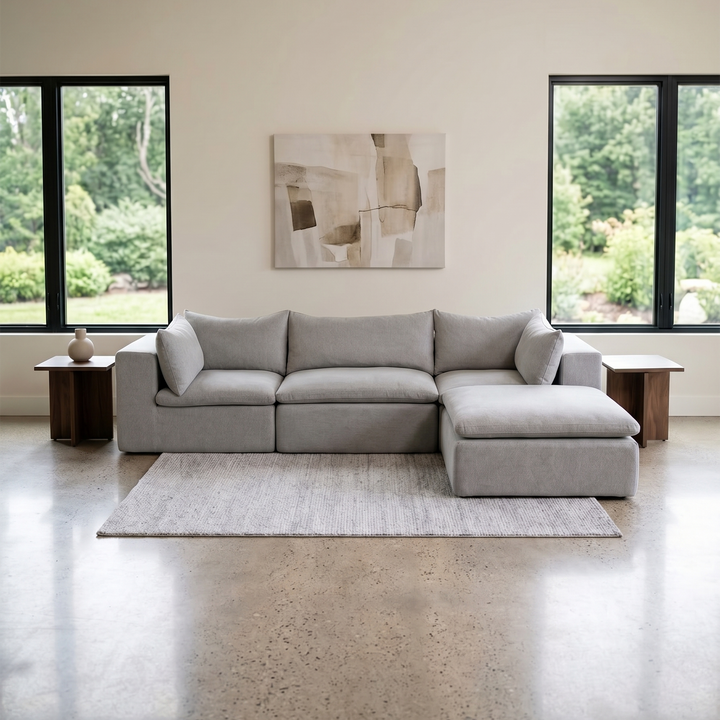 Gray sectional sofa in a modern living room with large windows and abstract art on the wall. 