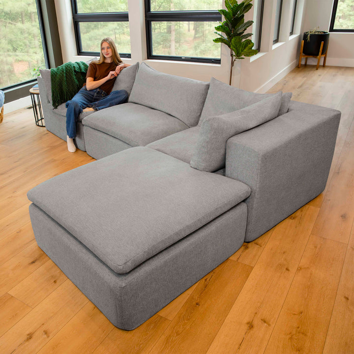 Gray sectional sofa in a room with large windows and a person sitting on it. 