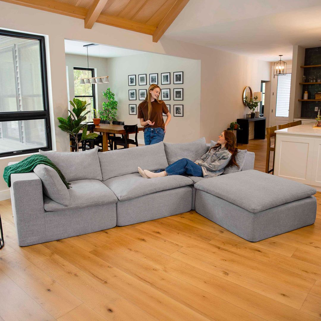 Living room with a gray sectional sofa, wooden floor, and people in the background. 