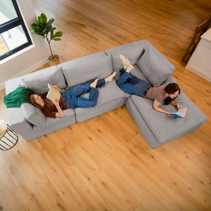 Two people lying on a gray sectional sofa in a living room with wooden flooring. 