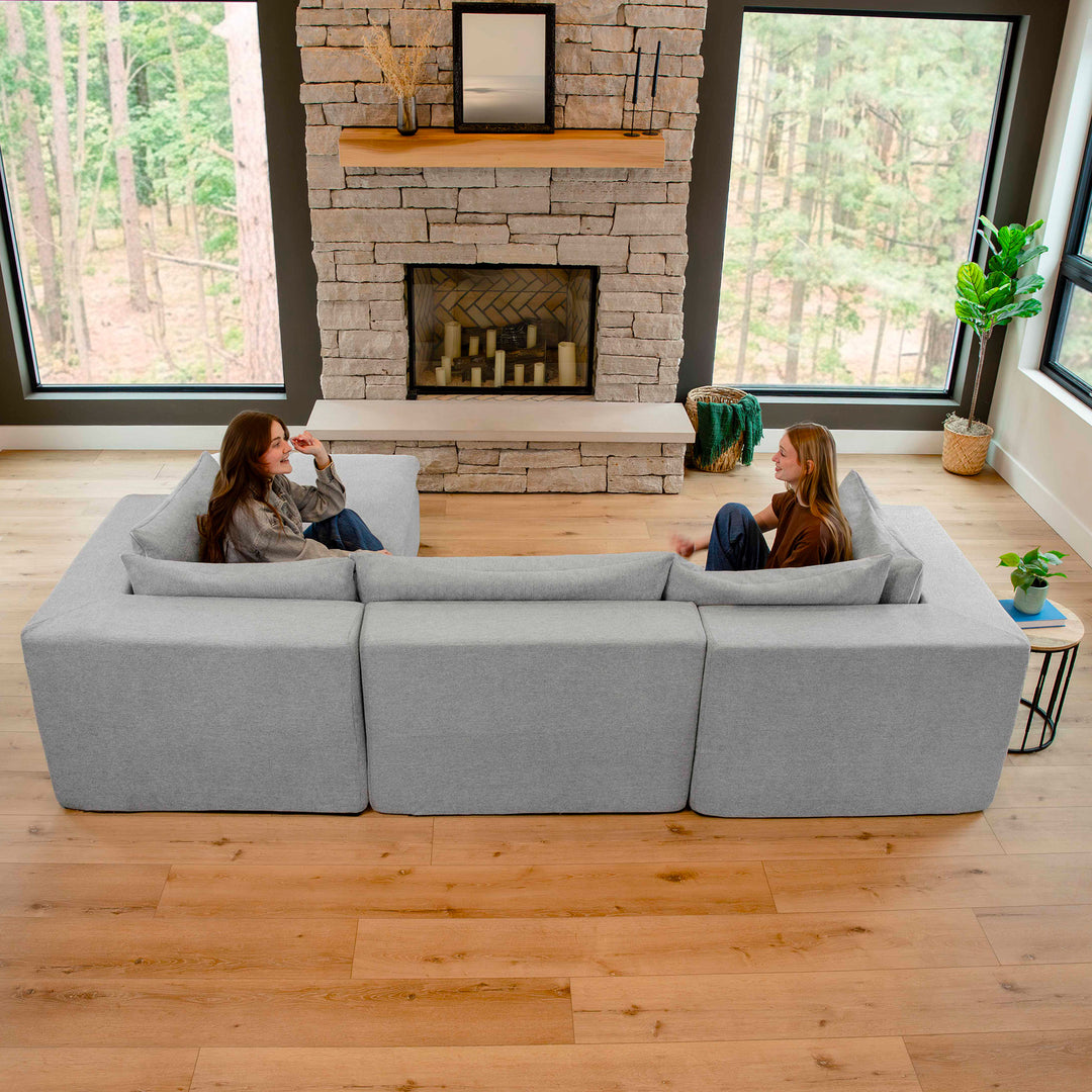 Two women sitting on a large sectional sofa in a modern living room with a stone fireplace. 