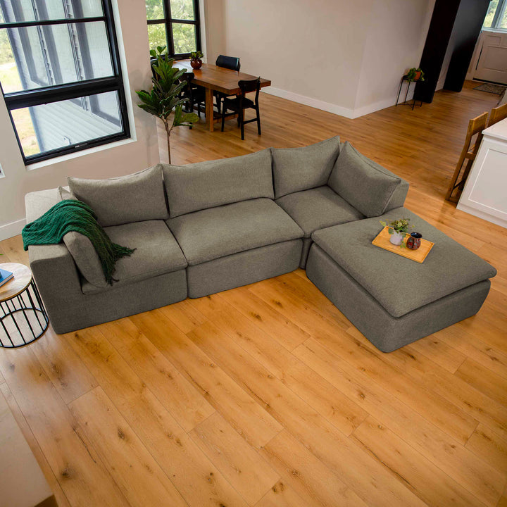 Gray sectional sofa in a living room with wooden flooring and a dining area in the background. 