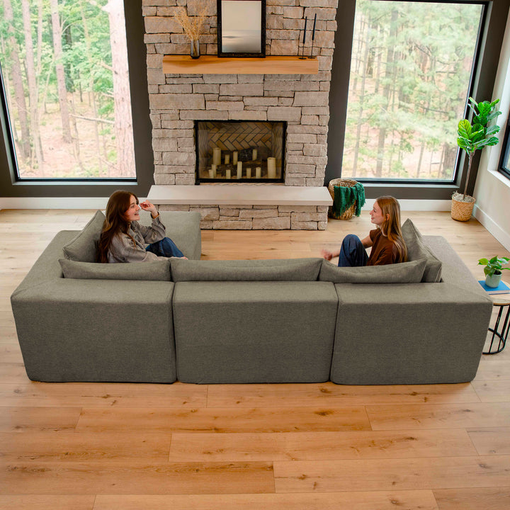 Two people sitting on a large gray sectional sofa in a modern living room with a stone fireplace. 
