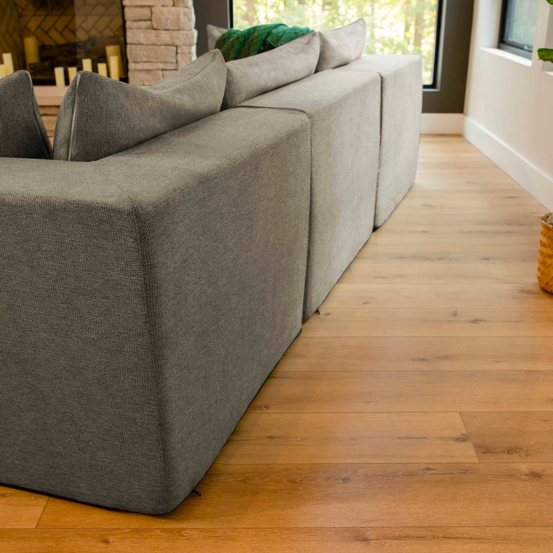 Gray sectional sofa in a living room with wooden floor and fireplace. 