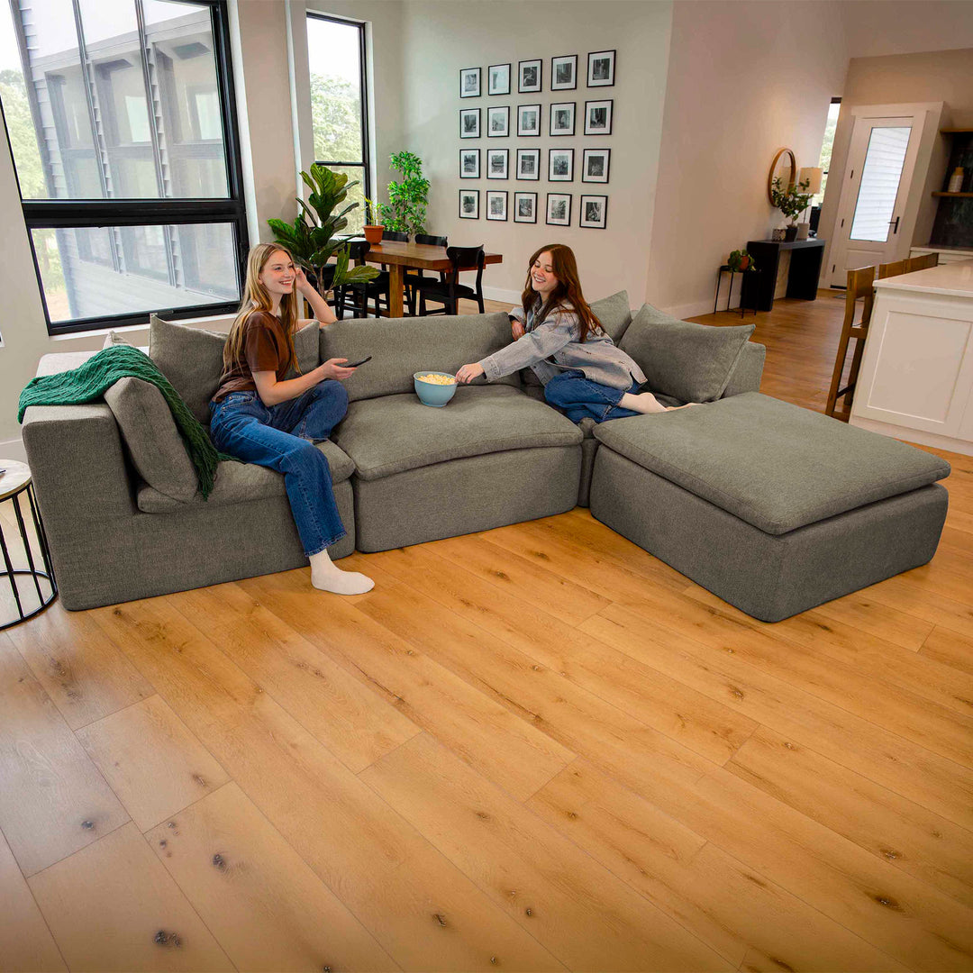 Two women sitting on a large gray sectional sofa in a modern living room. 