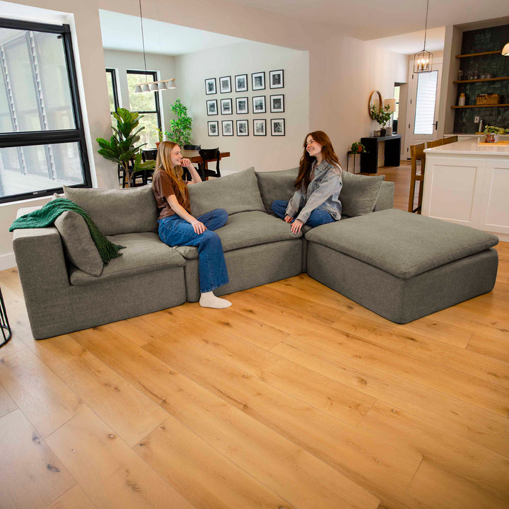 Two women sitting on a gray sectional sofa in a modern living room. 