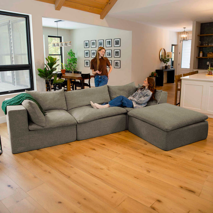 Living room with a gray sectional sofa, wooden floor, and people in the background. 