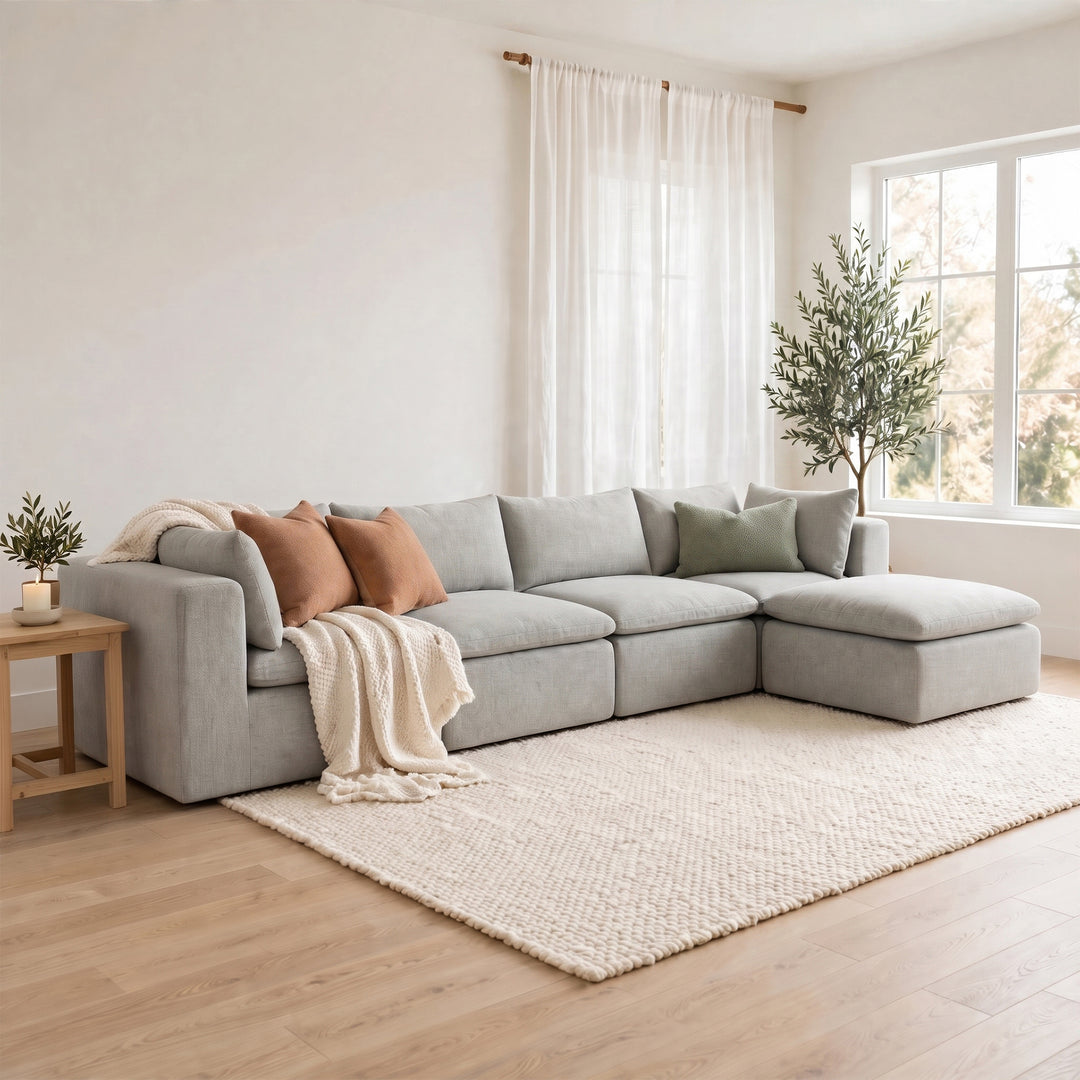 A light gray modular sectional sofa with a chaise lounge, styled in a bright, modern living room with a cream textured rug, wooden floor, and potted plants. 