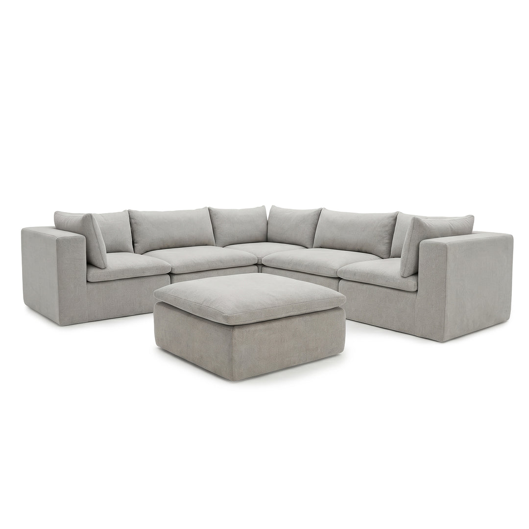 A light gray upholstered sectional sofa with matching square back cushions and a matching ottoman, shown on a plain white studio background. 