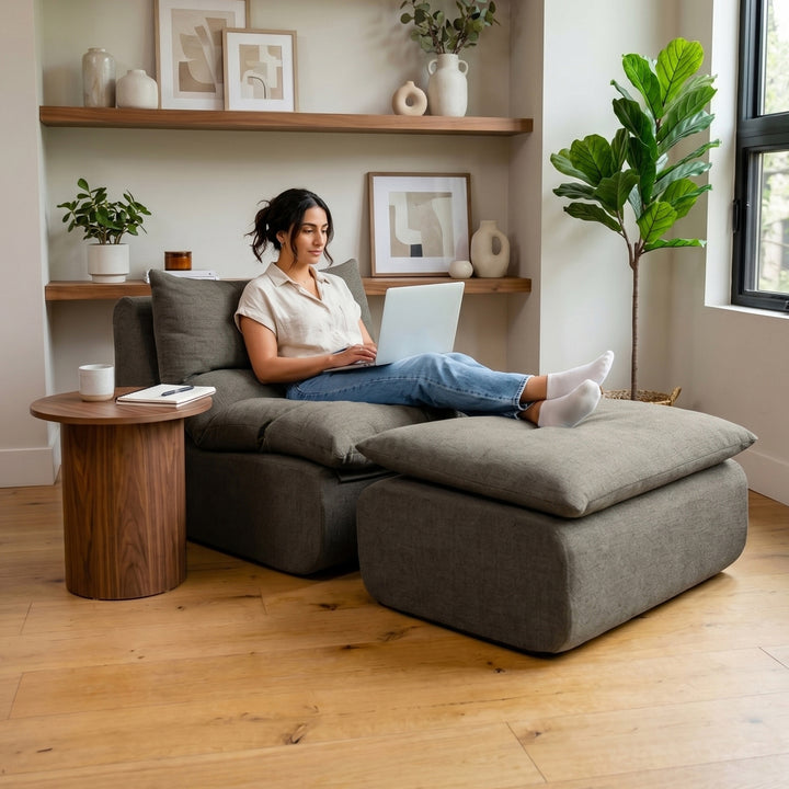 Woman sitting on a gray sectional sofa using a laptop in a cozy living room. 