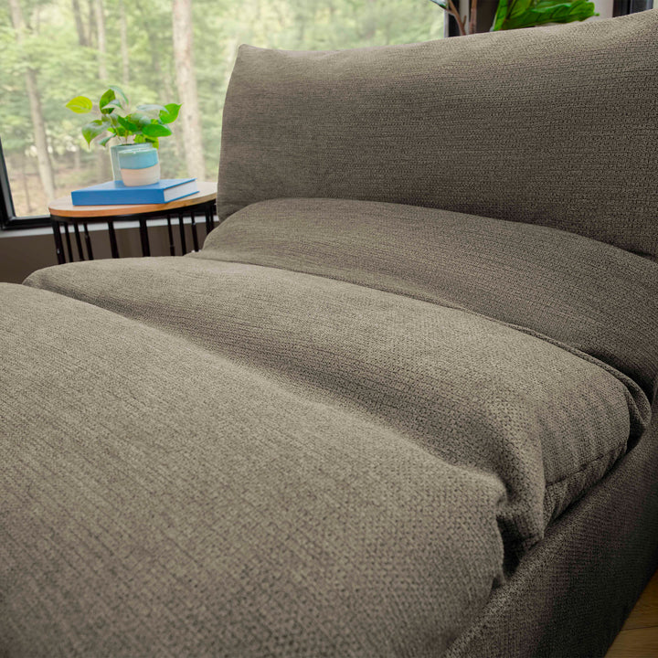 Gray textured comforter on a bed with a blurred background 