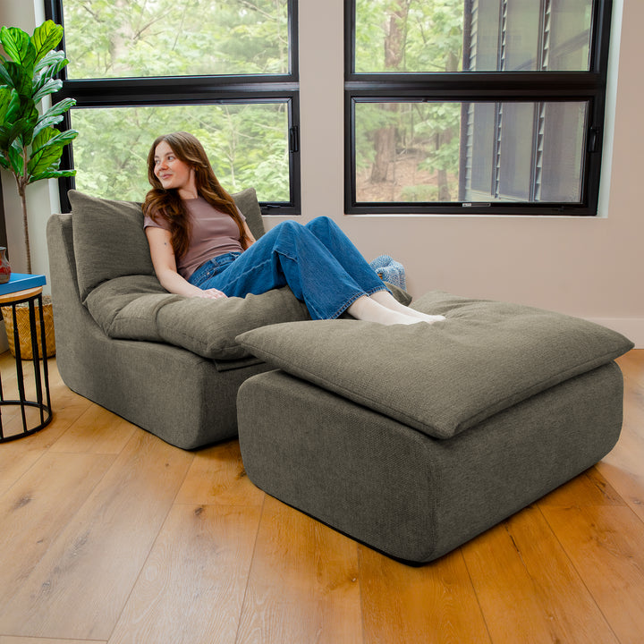Woman sitting on a large gray bean bag chair in a room with large windows. 