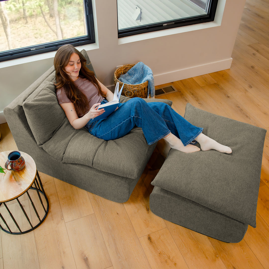 Person sitting on a gray sectional sofa reading a book in a cozy living room. 