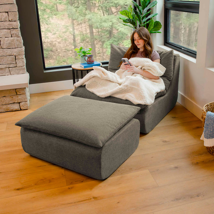 Woman sitting on a gray sectional sofa with a blanket, using a phone in a cozy living room. 