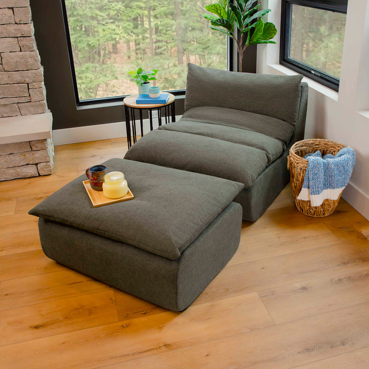 Gray floor sofa with ottoman in a room with wooden flooring and large windows. 