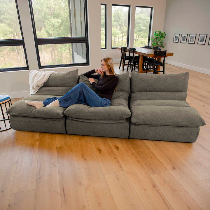 Woman sitting on  pillow-top sofa in the living room with windows and wood flooring. 
