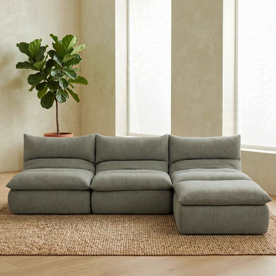 A modern sectional sofa in a muted sage green fabric, styled in a minimalist living room with a large potted fiddle-leaf fig plant on a woven jute rug. #color_misty-gray-terra-knit