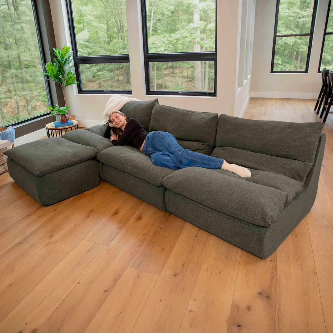 Woman laying down on a sectional sofa with ottoman that is on a wood floor 