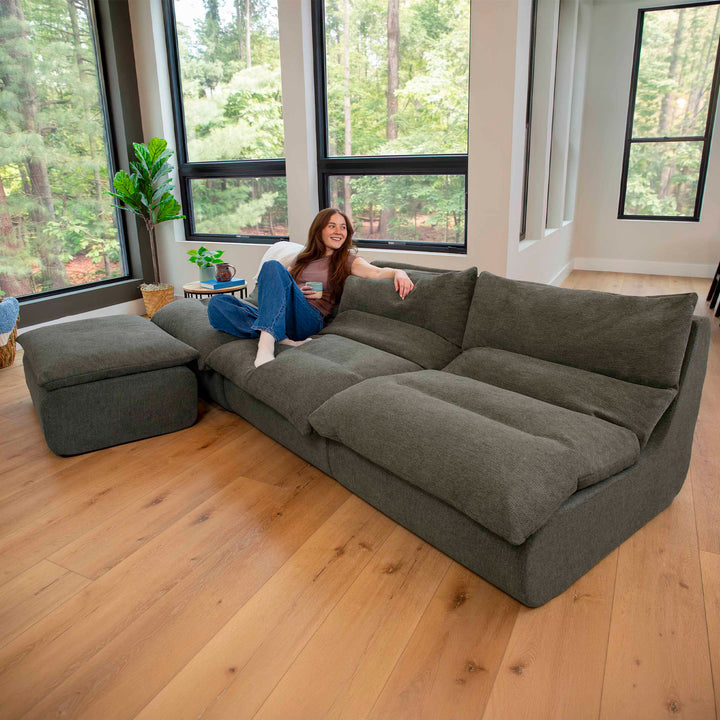 Driftscape sectional sofa with ottoman woman on sofa in a living room with big windows and wood flooring 