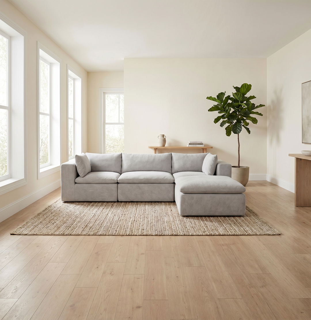 A light gray modular sectional sofa with a chaise lounge, styled in a bright, modern living room with light wood floors and a large woven area rug. #color_cottage-gray-terra-knit
