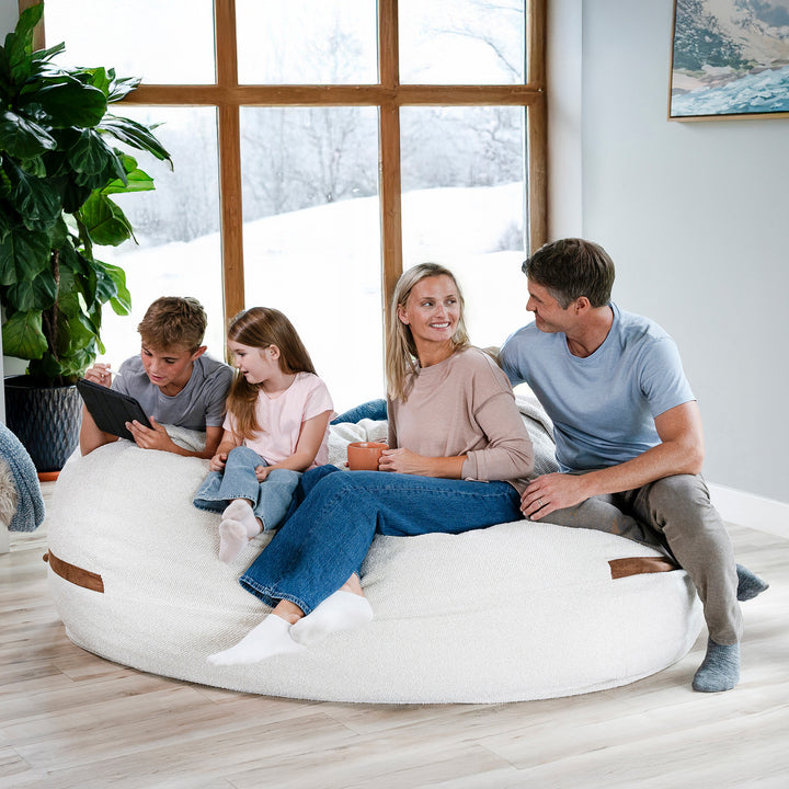 Family sitting on a large white bean bag in a bright room with large windows. #color_sandstone-textured-boucle