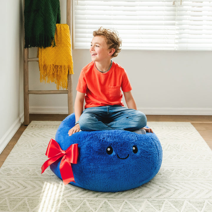Child sitting on a blue bean bag with a smiley face and red bow in a room.