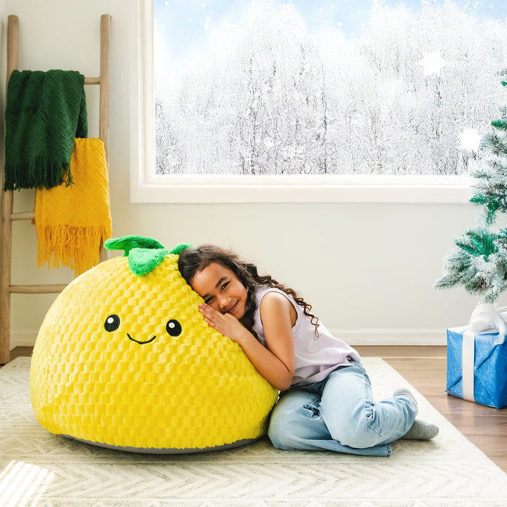 Child hugging a large yellow plush lemon-shaped pillow in a cozy room with a window and Christmas decorations.