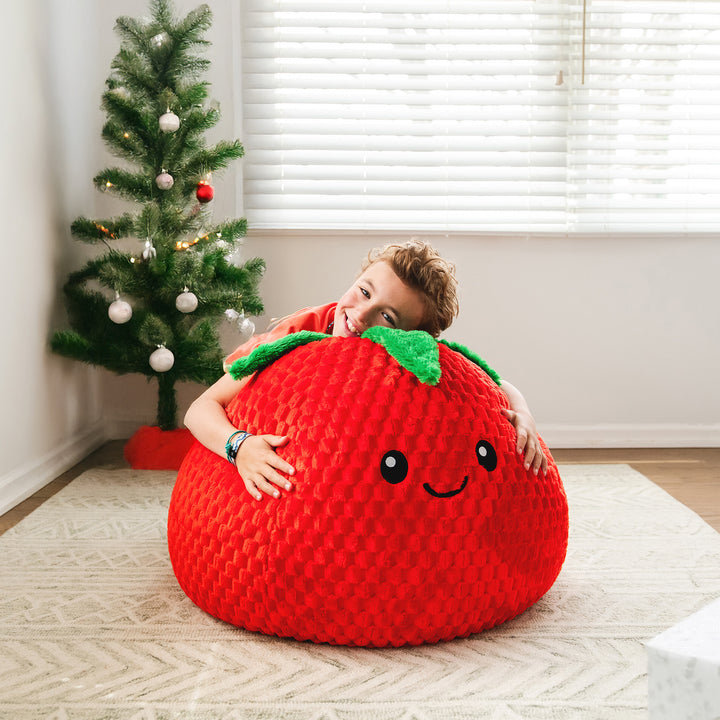 Child playing with a red bean bag shaped like a strawberry in a room with a Christmas tree.