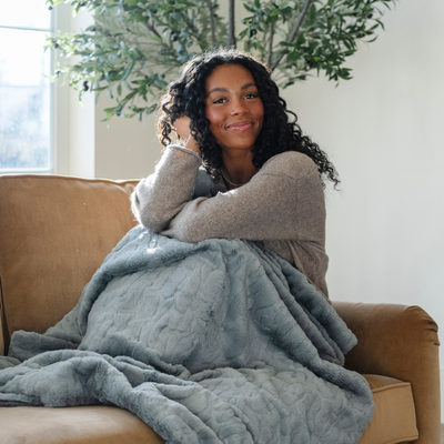 Woman sitting on a couch wrapped in a gray blanket with a plant in the background