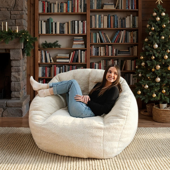 Woman sitting on a bean bag chair in a cozy room with bookshelves and a Christmas tree. #color_icing-teddy-boucle