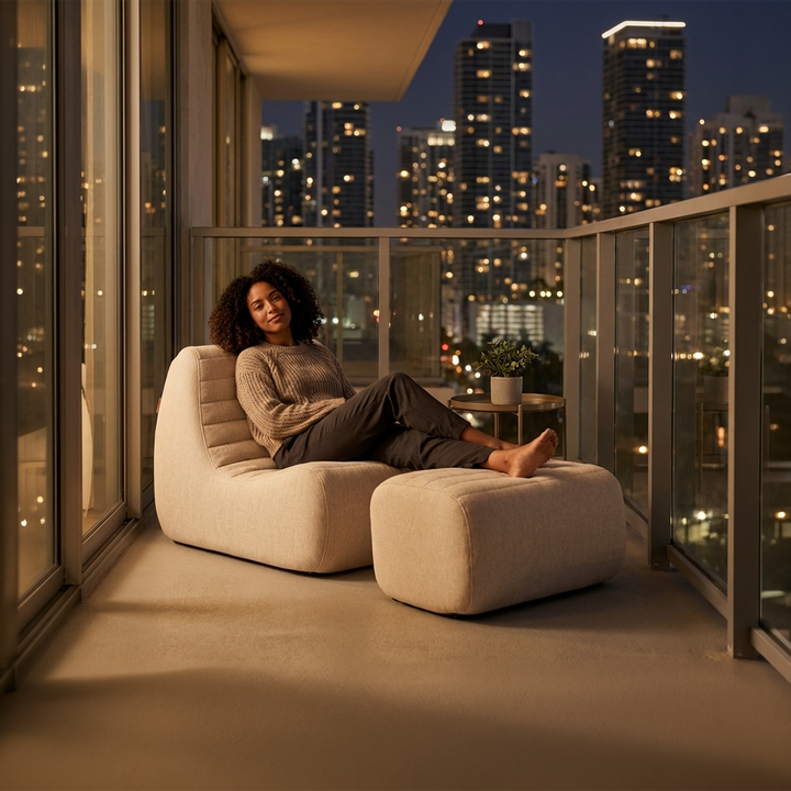 Woman sitting on a modern chair with a cityscape view at night. #color_sunlit-cream-outdoor-performance-linen